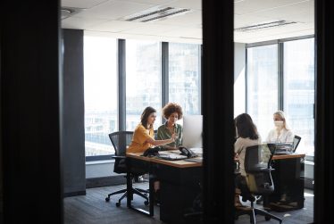 Four female creative colleagues busy working in an office, seen through glass wall with text on it